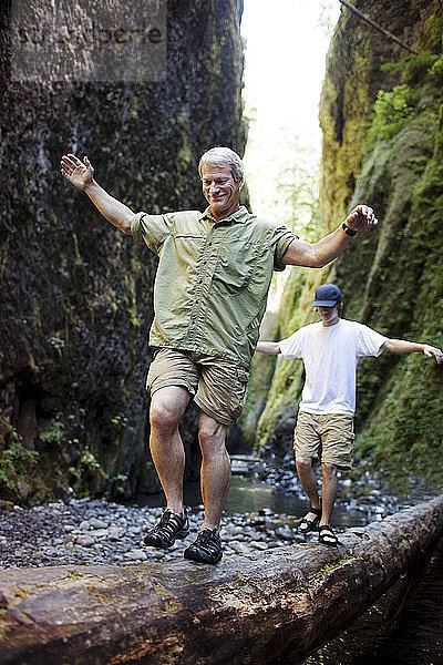 Vater und Sohn mit ausgestreckten Armen auf einem Baumstamm im Wald spazieren