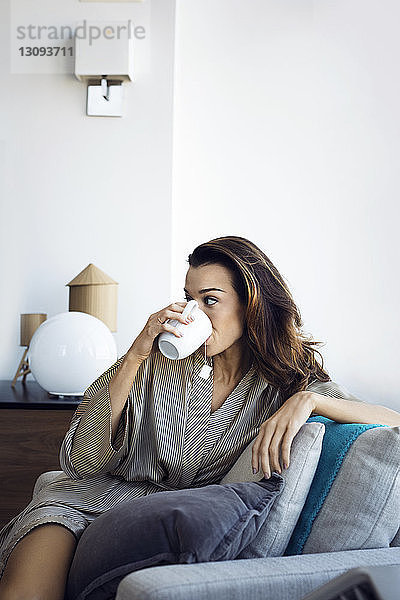 Frau trinkt Tee  während sie sich zu Hause auf einem Sessel entspannt