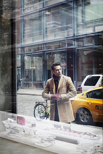 Mann steht auf Fußweg  gesehen durch Fenster im Laden