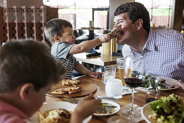 Junge  der seinen Vater im Restaurant mit Pizza füttert