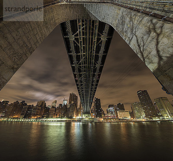 Tiefblick auf die Queensboro-Brücke über den East River bei bewölktem Himmel in der Nacht