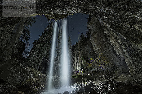 Rückansicht eines Silhouettenmannes  der nachts am Wasserfall im Wald steht