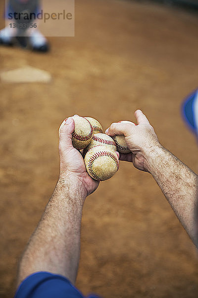 Ausgeschnittenes Bild eines Trainers  der Basebälle auf dem Spielfeld hält