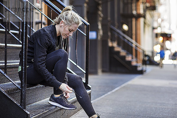 Sportlerin bindet Schnürsenkel  während sie auf Stufen in der Stadt sitzt
