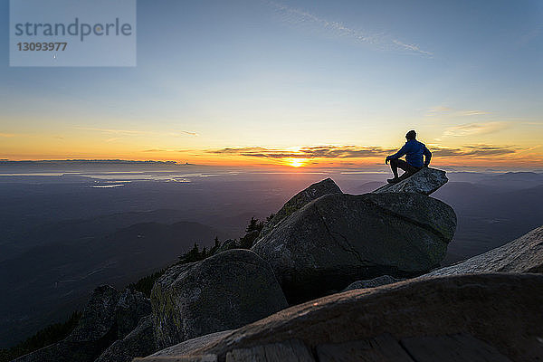 Mann sitzt bei Sonnenuntergang im Mount Pilchuck State Park auf einem Felsen gegen den Himmel