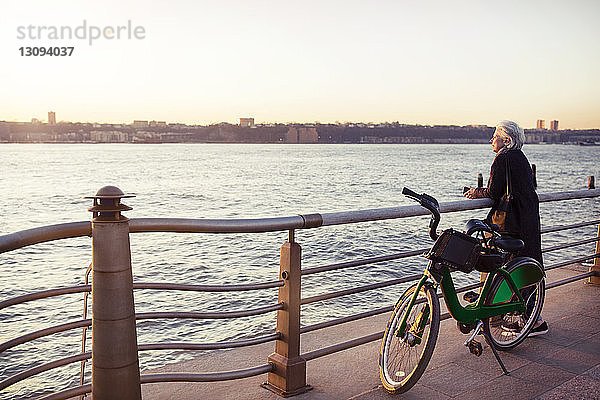 Ältere Frau mit Blick aufs Meer  während sie auf der Promenade mit dem Fahrrad steht