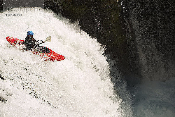 Mann im Kajak auf einem Wasserfall auf einem Fluss