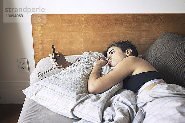 Frau benutzt Mobiltelefon beim Entspannen im Bett