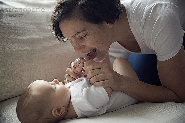 Glückliche Mutter spielt mit dem zu Hause auf dem Sofa liegenden Sohn