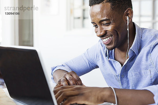 Glücklicher Mann hört Musik  während er zu Hause einen Laptop benutzt