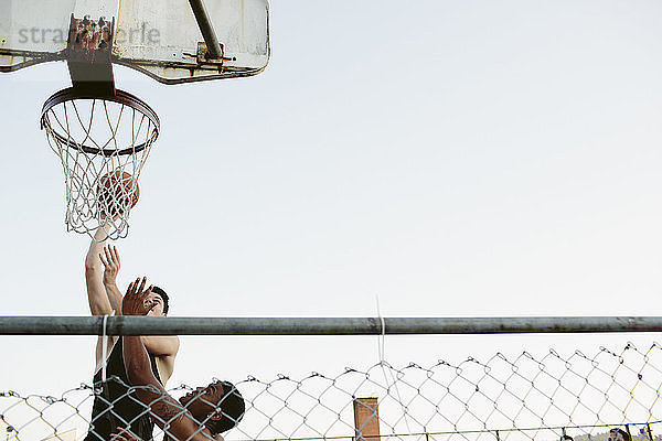 Niedrigwinkelansicht von Freunden beim Basketballspielen gegen klaren Himmel