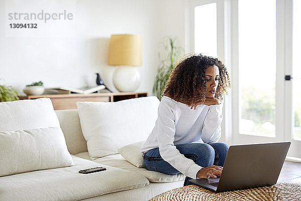 Frau benutzt Laptop-Computer  während sie zu Hause auf dem Sofa sitzt