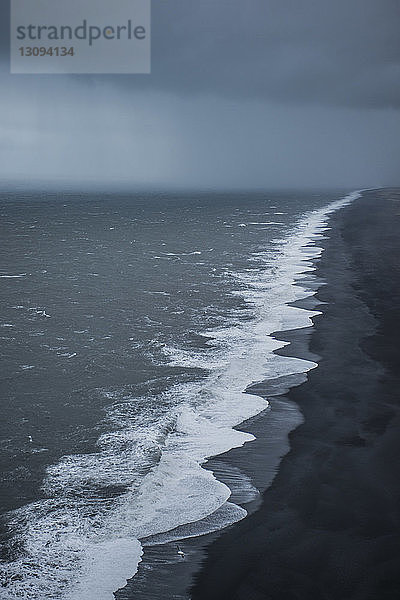 Szenische Ansicht der Wellen am Schwarzen Sandstrand vor stürmischen Wolken
