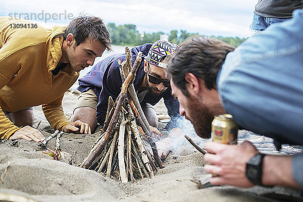 Männliche Freunde bereiten ein Lagerfeuer im Sand am Flussufer