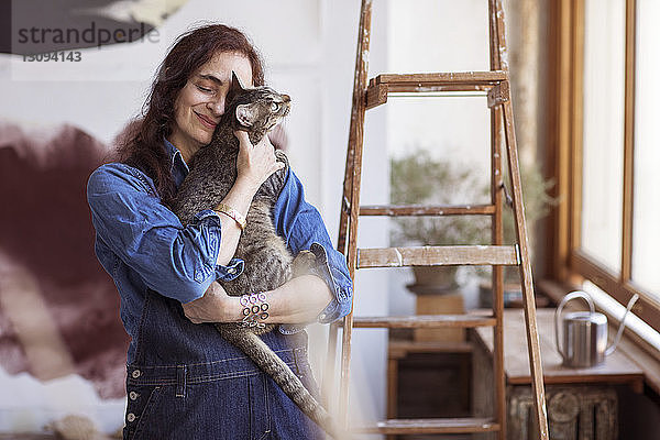 Lächelnder Künstler umarmt Katze  während er im Workshop steht