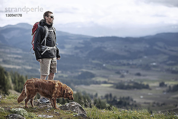 Wanderer mit Hund auf Berg gegen Himmel stehend