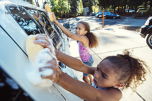 Hochwinkelaufnahme von Mädchen  die in der Einfahrt ein Auto waschen