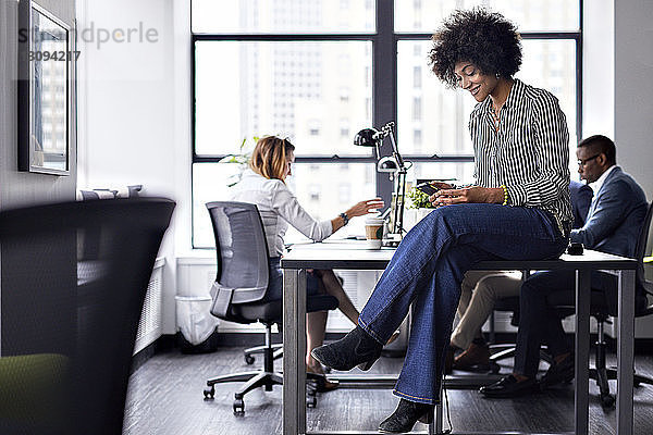 Geschäftsfrau benutzt Smartphone  während Kollegen im Hintergrund arbeiten