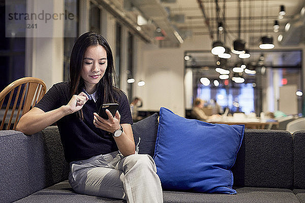 Selbstbewusster Unternehmer benutzt Mobiltelefon  während er im Kreativbüro auf dem Sofa sitzt