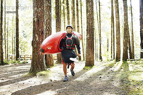 Mann trägt Kajak beim Waldspaziergang