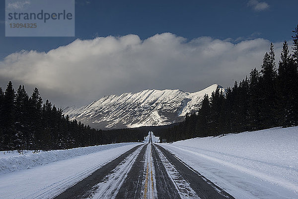 Schneebedeckte Straße gegen Berge und bewölkten Himmel