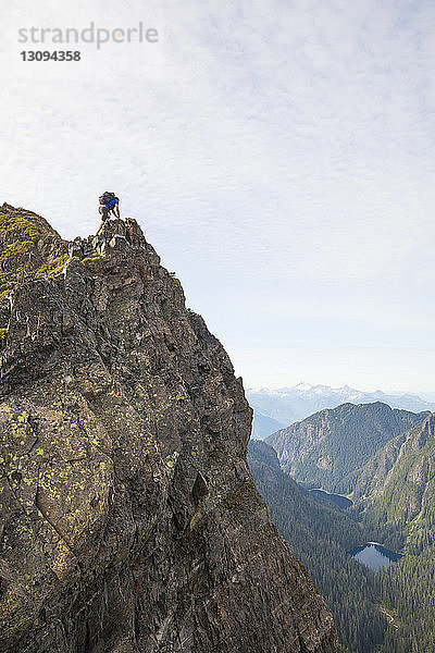 Niedrigwinkelansicht eines sorglosen Wanderers mit Rucksack auf dem Berg gegen den Himmel