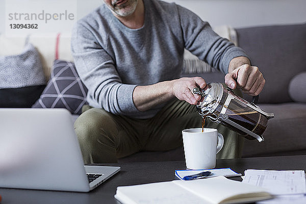 Ein Mann gießt zu Hause Kaffee aus der französischen Presse in eine Tasse