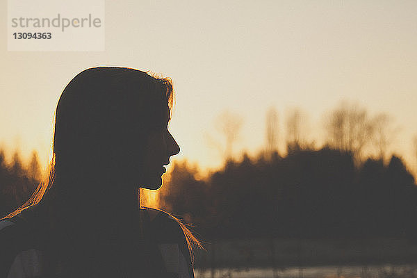 Silhouette einer Teenagerin  die bei Sonnenuntergang gegen den klaren Himmel wegschaut