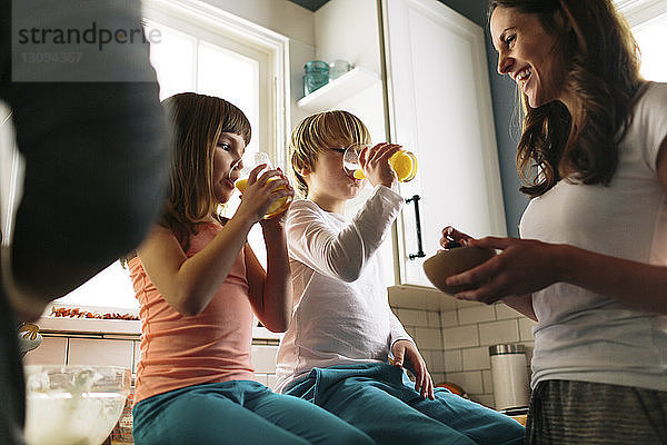 Mutter betrachtet Kinder  die Saft trinken  während sie auf der Küchentheke sitzt