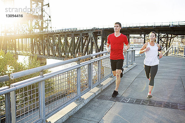 Freunde joggen gemeinsam auf der Brücke gegen den klaren Himmel