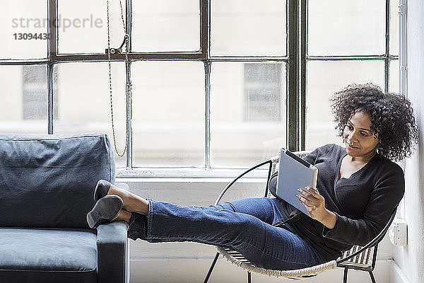 Geschäftsfrau benutzt digitales Tablet  während sie im Büro auf einem Stuhl ruht