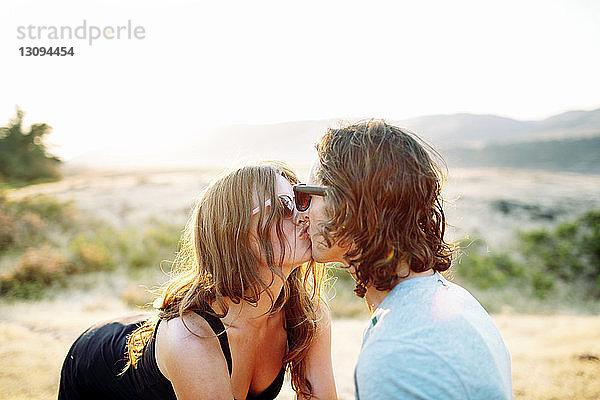 Glückliches Paar küsst sich auf dem Feld vor klarem Himmel