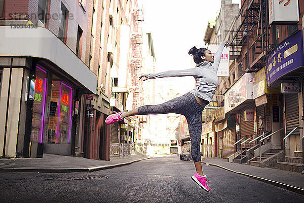 Weibliche Joggerin springt auf der Straße inmitten von Gebäuden