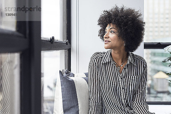 Nachdenkliche Geschäftsfrau schaut durch das Fenster  während sie im Büro sitzt