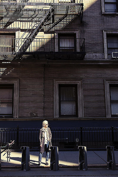 Ältere Frau steht auf dem Bürgersteig vor dem Gebäude