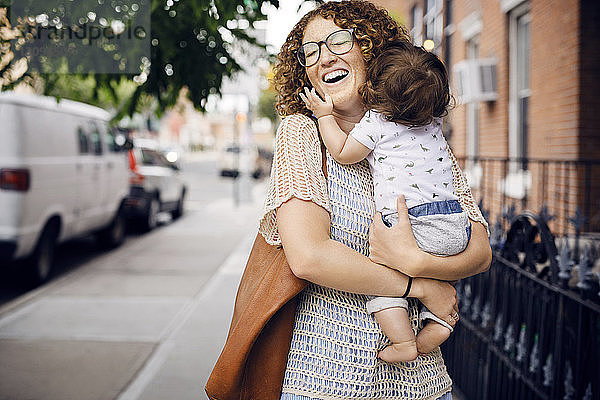 Fröhliche Mutter trägt einen kleinen Jungen auf einem Fußweg in der Stadt