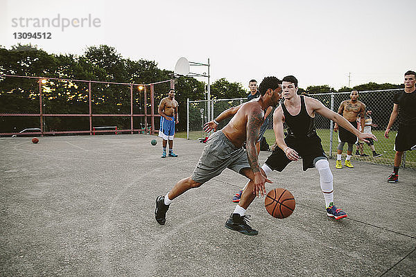 Männliche Freunde spielen Basketball auf dem Platz gegen den klaren Himmel