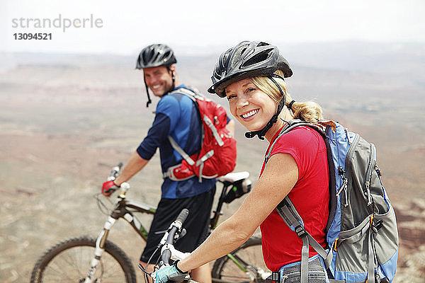 Porträt eines lächelnden Paares  das mit Fahrrädern auf einer Klippe steht