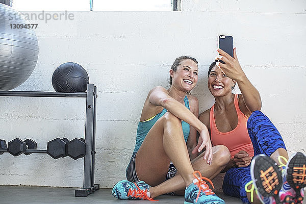 Glückliche Freundinnen  die sich im Fitnessstudio per Mobiltelefon selbstständig machen