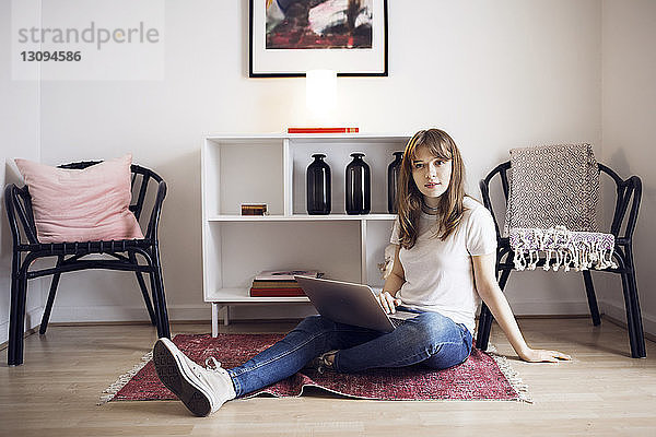 Porträt einer jungen Frau  die zu Hause mit Laptop auf dem Boden sitzt