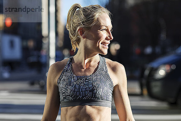 Weibliche Sportlerin schaut weg  während sie an einem sonnigen Tag auf der Straße steht