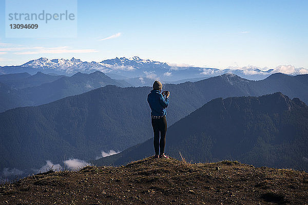 Rückansicht einer Frau  die an einer Klippe vor Bergen fotografiert