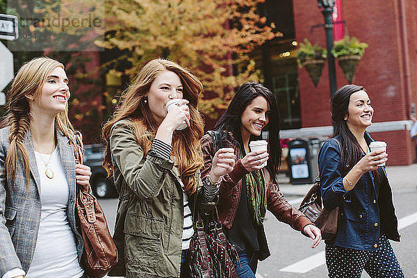 Glückliche Freundinnen trinken Kaffee beim Spaziergang auf der Straße