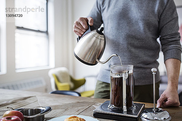 Ein Mann gießt Wasser in die französische Presse  während er zu Hause Kaffee kocht