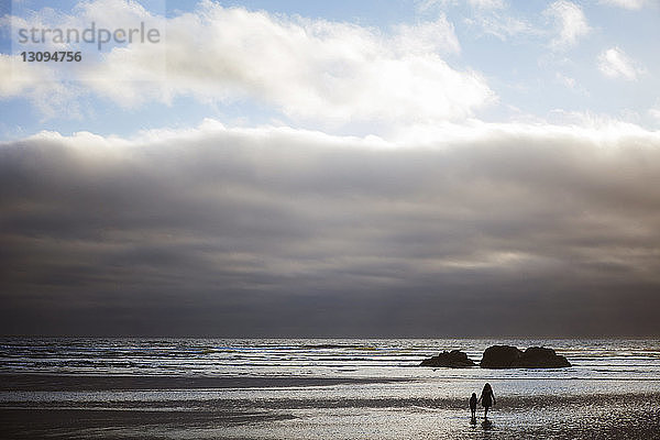 Mutter und Tochter spazieren am Strand vor bewölktem Himmel