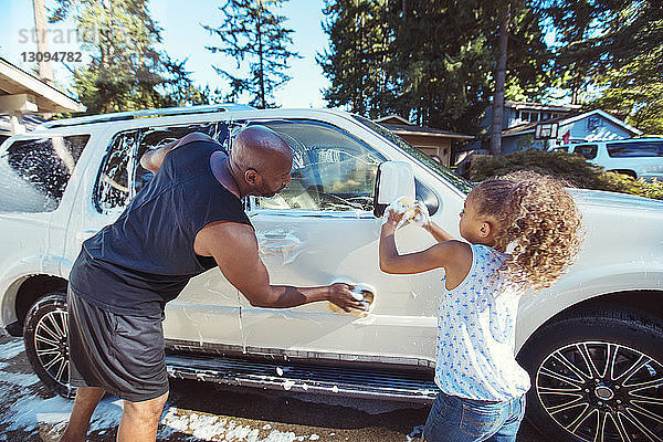 Vater und Tochter waschen Auto in Einfahrt