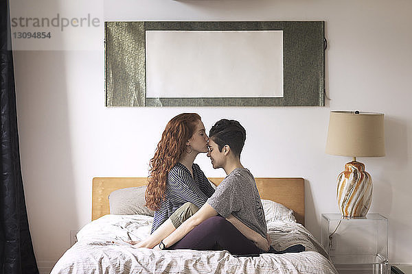 Romantische Lesbe küsst zu Hause auf die Stirn ihrer Freundin  während sie auf dem Bett sitzt