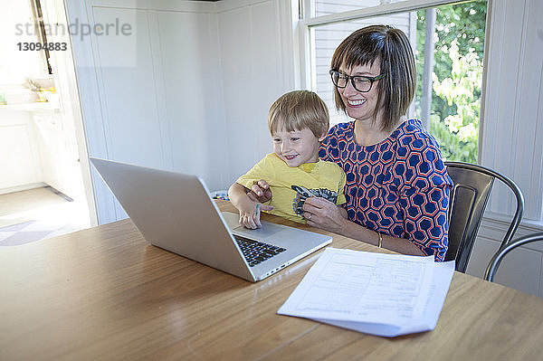 Lächelnde Mutter mit Sohn benutzt Laptop-Computer auf dem Tisch zu Hause