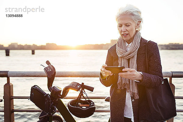 Ältere Frau benutzt Smartphone mit dem Fahrrad gegen das Meer