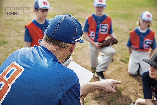 Rückansicht des Trainers  der während der Diskussion mit dem Baseballteam auf dem Spielfeld zeigt